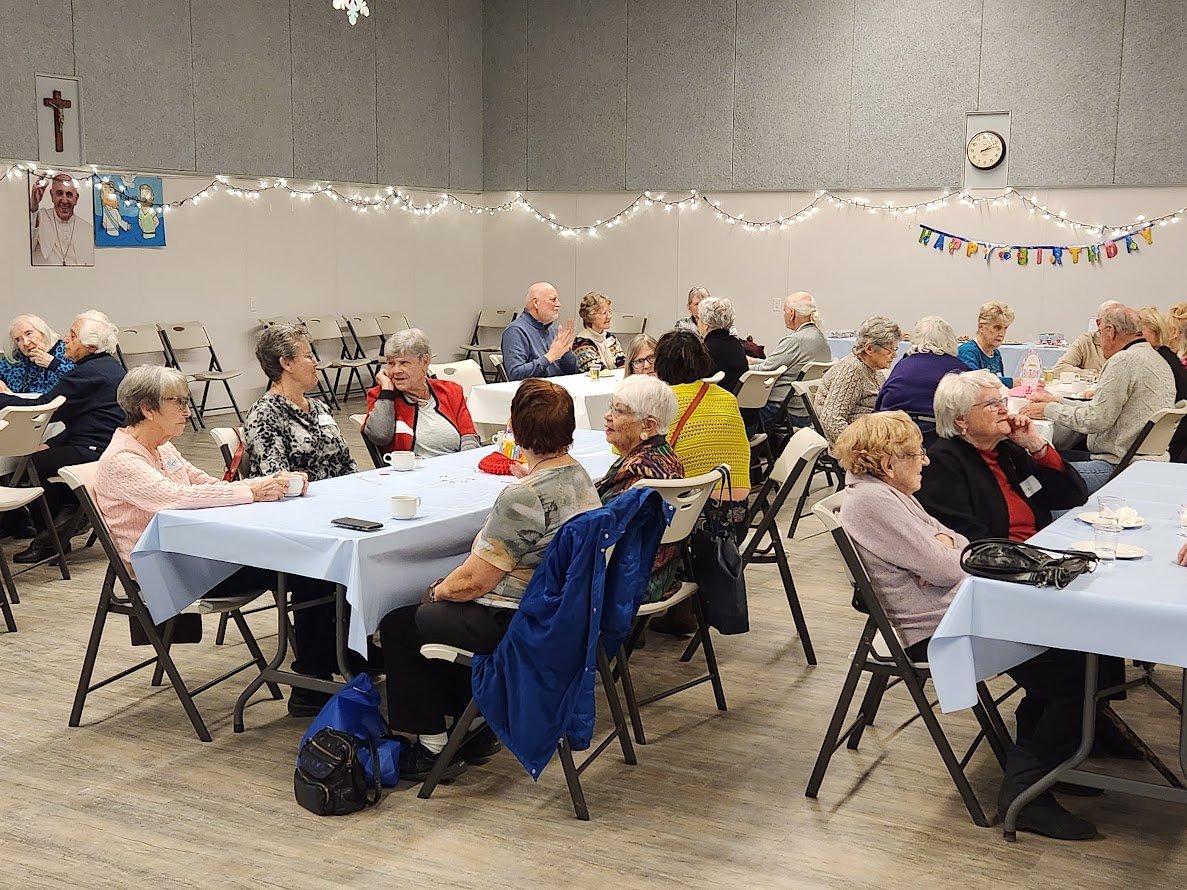 Picture of a Maturing Adult program with attendees at tables and chairs in the hall enjoying everyone's birthday party